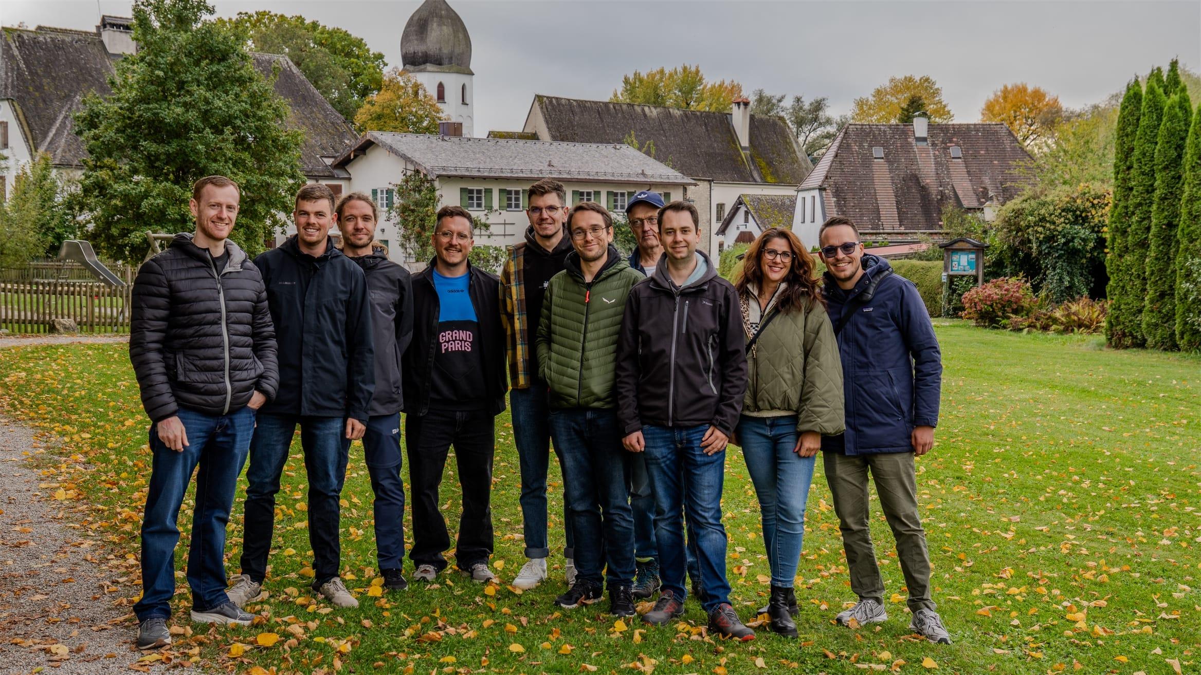 Das Miragon-Team als Gruppe auf einer Wiese vor einem Dorf mit Kirchturm